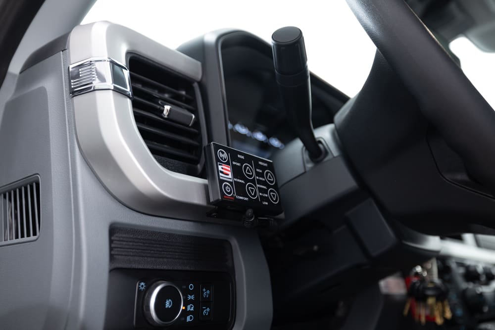 Close-up of a Demers ambulance cab dashboard showing an auxiliary control panel mounted near the steering column, with air vents and driver lighting controls within easy reach