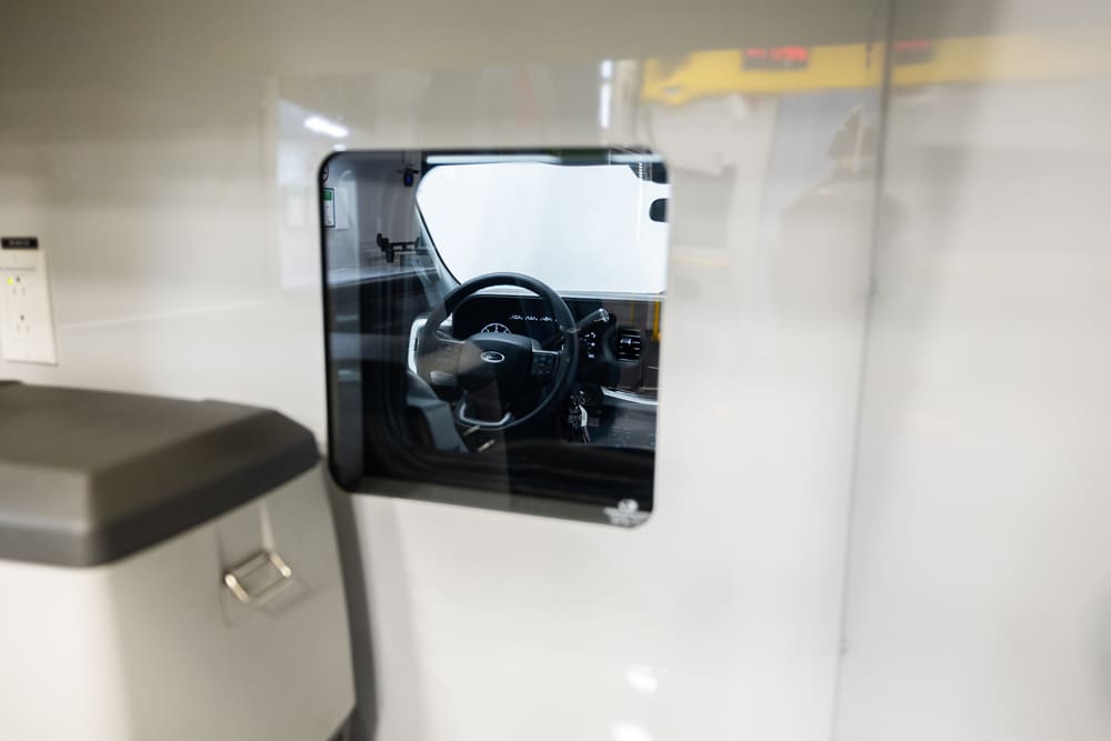 Demers ambulance cab-to-patient compartment pass-through window providing clear visibility to the driver area, with steering wheel visible through the sealed interior glass