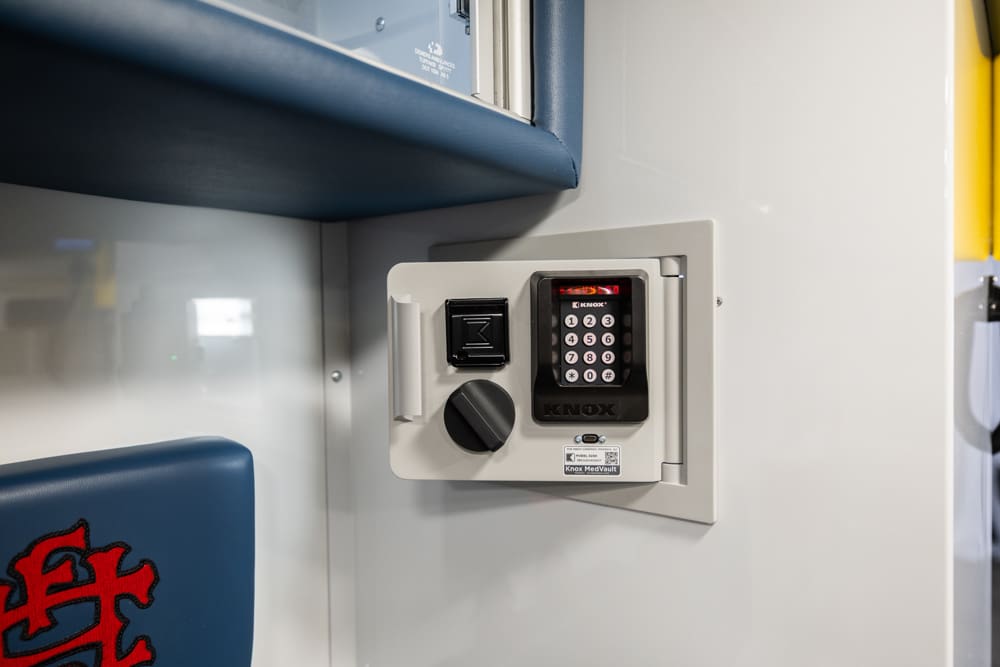 Close-up of a Demers ambulance interior secure medication safe with keypad lock, rotary handle, and integrated power switch mounted within the patient compartment cabinetry