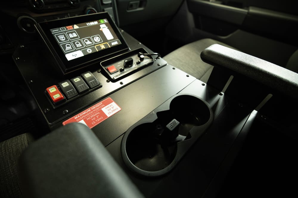 Close-up of a Demers ambulance center console showing an integrated touchscreen control panel, rocker switches, cup holders, and armrest