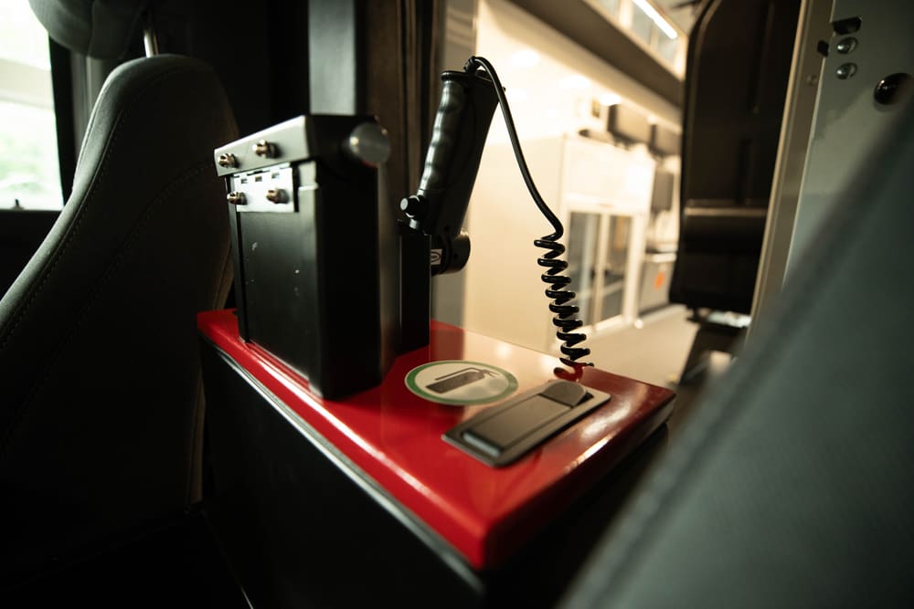 Close-up of a Demers ambulance interior showing a handheld control microphone mounted on a compact red console between seats, positioned for quick access by the crew