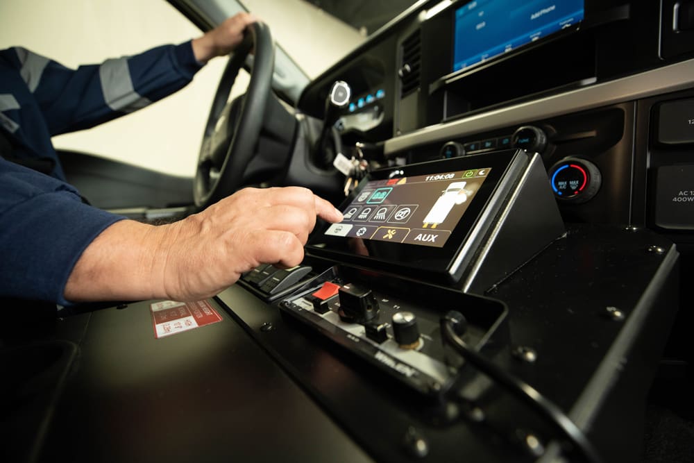 Close-up of a Demers ambulance cab showing a driver using a touchscreen control panel on the center console to manage vehicle and patient-module systems