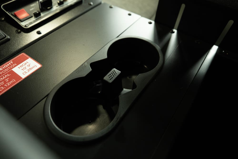 Close-up of a Demers ambulance cab center console showing a dual cup holder integrated into a rugged, matte-finish control surface next to vehicle control switches