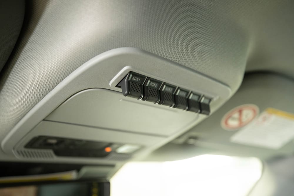 Close-up of a Demers ambulance cab overhead console with labeled auxiliary rocker switches integrated into the headliner for easy driver access