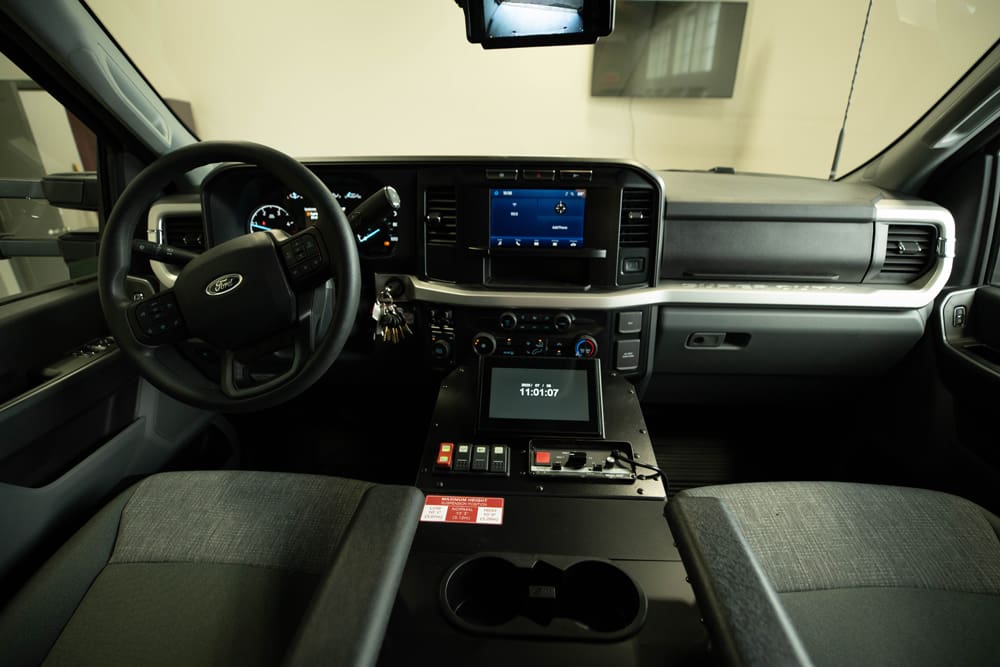 Wide view of the Demers ambulance cab interior showing the driver and passenger seats, steering wheel, center console with integrated touchscreen controls, and dashboard layout
