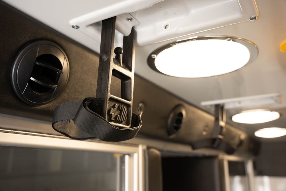 Close-up of an adjustable ceiling-mounted IV hook and strap inside the Demers ambulance patient compartment, positioned near overhead lighting and air vents for secure IV support during transport