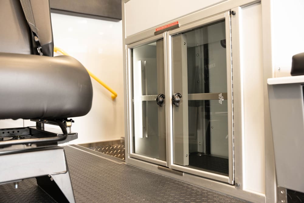 Sliding glass storage cabinet inside a Demers ambulance patient compartment, positioned below the squad bench for quick visibility and secure access to medical supplies during transport