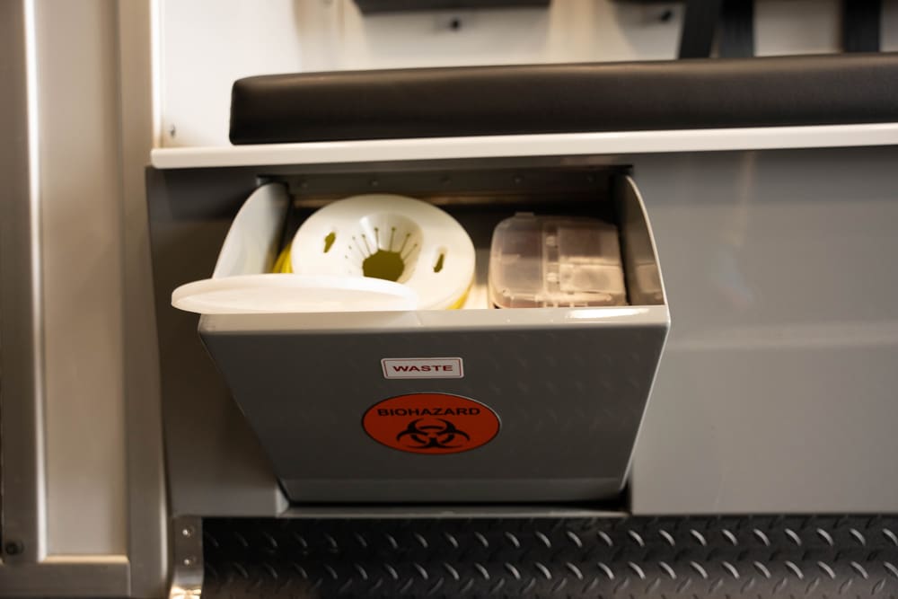 Built-in biohazard waste container inside a Demers ambulance, integrated beneath the seating area for safe, accessible disposal of medical waste during transport