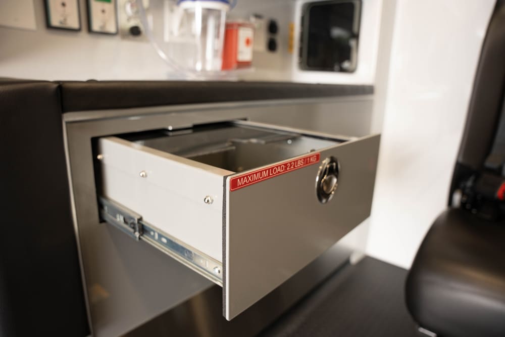 Close-up of an open aluminum storage drawer in a Demers ambulance patient compartment, showing smooth slide rails and a labeled maximum load capacity for organized, secure in-transit storage