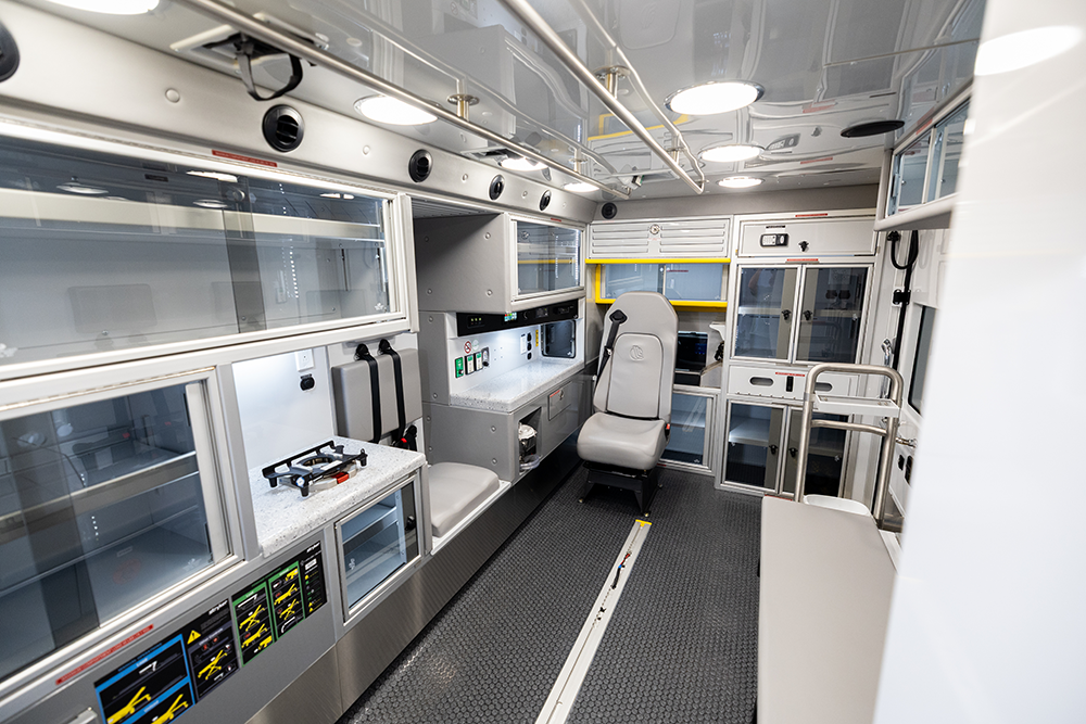 Interior view of a Demers ambulance patient compartment with cabinetry, overhead lighting, and a forward-facing attendant seat