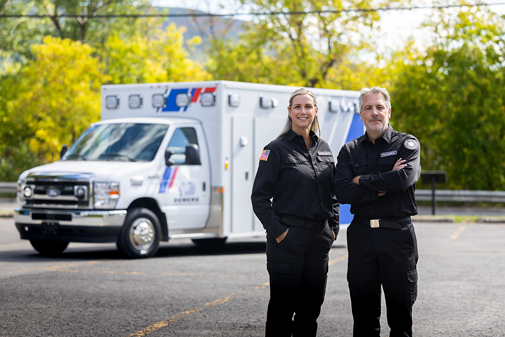 Two EMS professionals standing outdoors in a parking lot with a Demers ambulance in the background