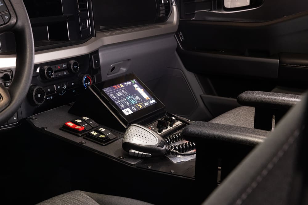 Demers ambulance cab center console featuring a touchscreen control panel, emergency light switches, climate controls, radio microphone, and integrated armrests between the front seats