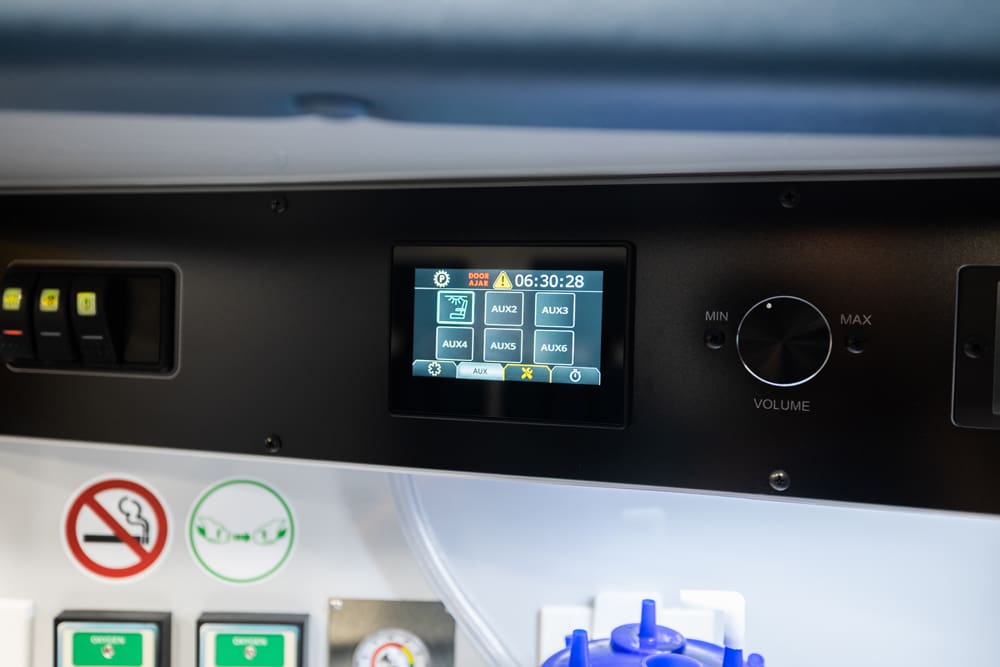 Demers ambulance interior control panel with touchscreen AUX system display, volume knob, and overhead switches mounted above medical gas outlets and safety signage