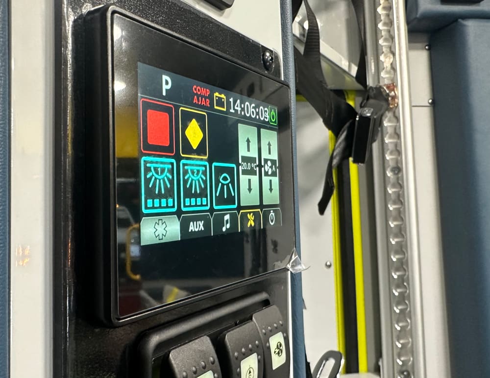 Close-up of a Demers ambulance touchscreen control panel displaying lighting, HVAC, and auxiliary system controls mounted beside the rear door inside the patient module