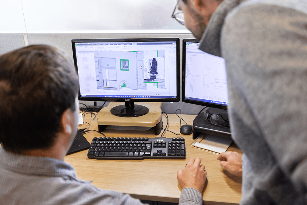 Two Demers engineers review ambulance interior CAD drawings on dual computer monitors, collaborating on design details at a workstation
